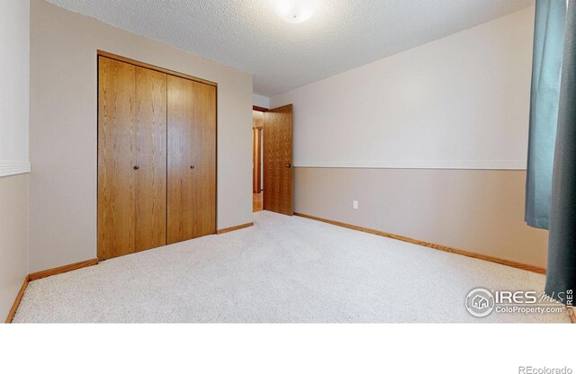 unfurnished bedroom with a closet, a textured ceiling, carpet, and baseboards