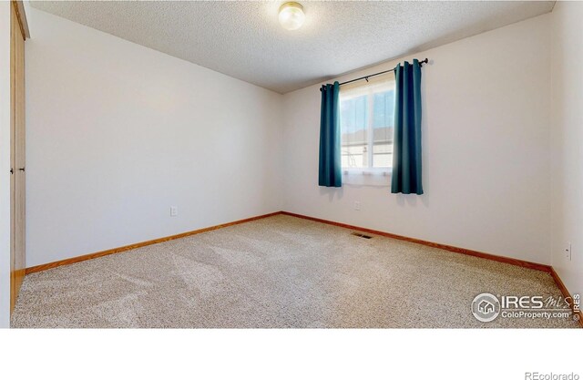 empty room featuring carpet flooring, a textured ceiling, baseboards, and visible vents