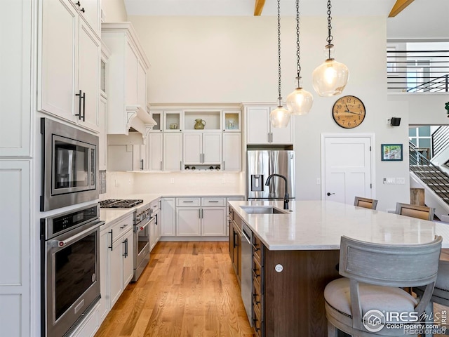 kitchen with a kitchen breakfast bar, a sink, glass insert cabinets, stainless steel appliances, and an island with sink