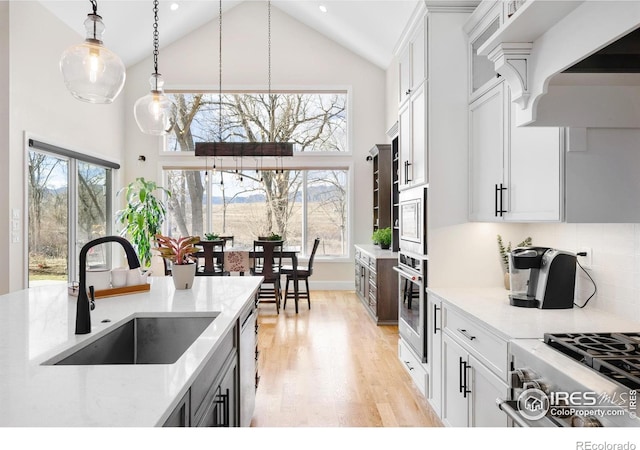 kitchen featuring appliances with stainless steel finishes, a sink, light wood-style floors, high vaulted ceiling, and pendant lighting