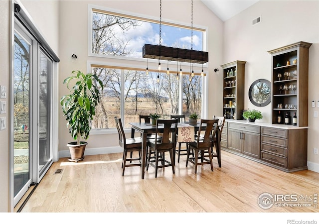 dining room featuring visible vents, light wood-style flooring, baseboards, and high vaulted ceiling