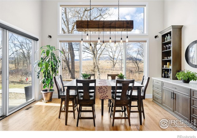dining room with plenty of natural light, light wood-type flooring, visible vents, and a towering ceiling