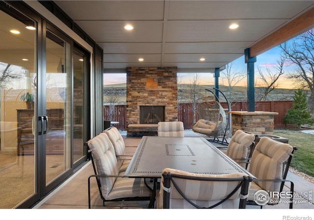 patio terrace at dusk with an outdoor stone fireplace, fence, and outdoor dining space