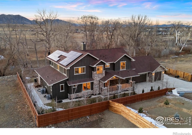 view of front of home with stone siding, a fenced backyard, a chimney, board and batten siding, and roof mounted solar panels