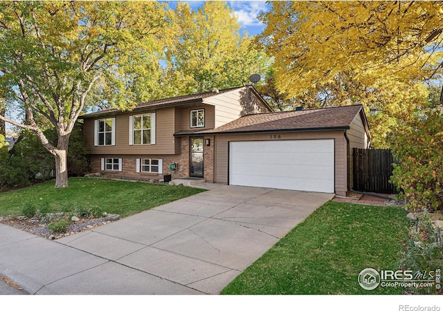 tri-level home featuring fence, a front yard, brick siding, an attached garage, and driveway
