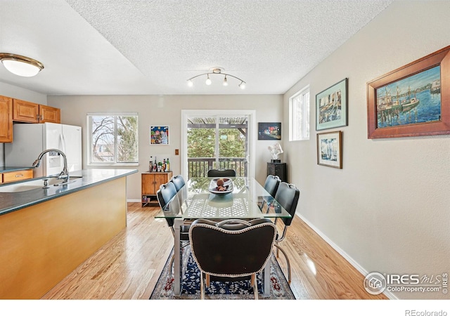dining area with baseboards, a textured ceiling, and light wood finished floors