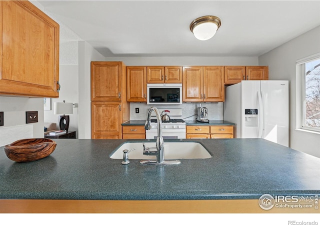 kitchen featuring brown cabinetry, dark countertops, white appliances, tasteful backsplash, and a sink