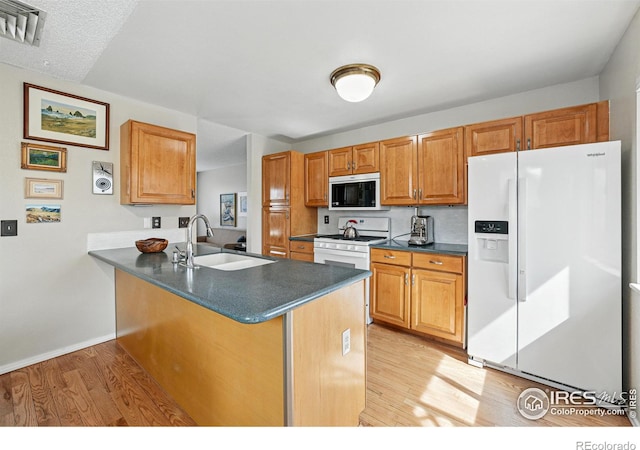 kitchen featuring dark countertops, a sink, a peninsula, white appliances, and light wood-style flooring