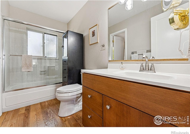 full bathroom featuring vanity, bath / shower combo with glass door, toilet, and wood finished floors