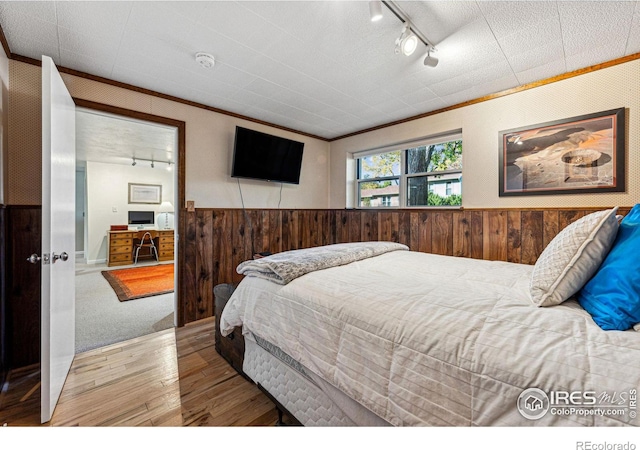 bedroom featuring crown molding, wood walls, rail lighting, wood finished floors, and a wainscoted wall