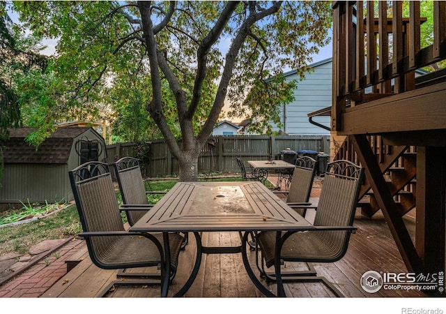 wooden deck featuring an outbuilding, outdoor dining space, a fenced backyard, and a storage unit