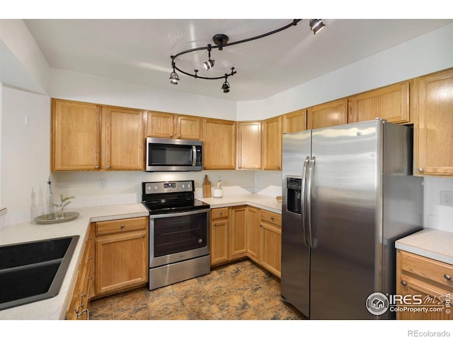 kitchen with light countertops, a sink, stone finish flooring, and stainless steel appliances