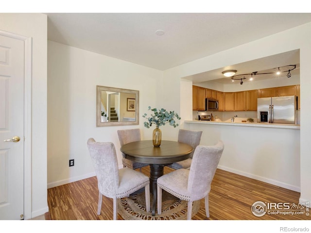dining room featuring baseboards, light wood-style flooring, and track lighting