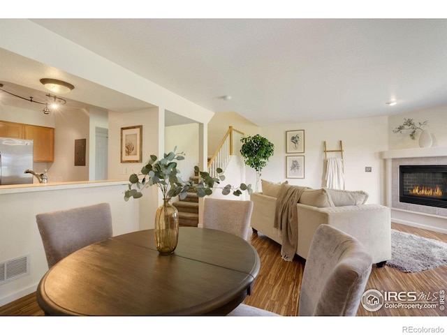 dining space featuring visible vents, wood finished floors, stairway, and a tile fireplace