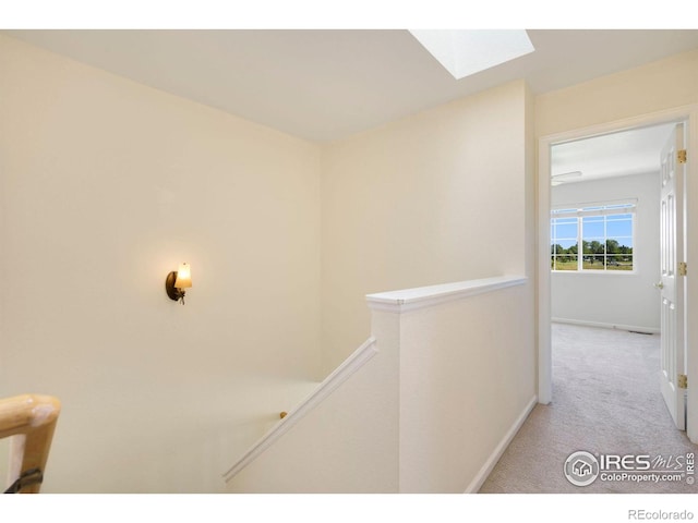 hall with light colored carpet, a skylight, an upstairs landing, and baseboards
