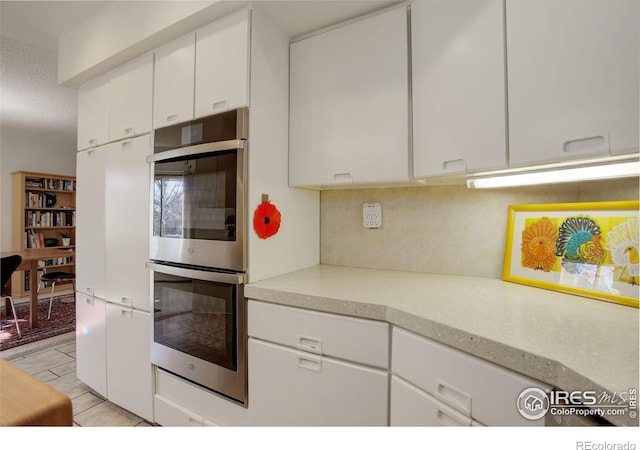 6611 Lakeview Dr, Boulder, CO 80303 - kitchen with stainless steel double oven, light tile patterned flooring, white cabinets, and tasteful backsplash