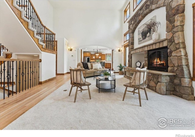 living room featuring a high ceiling, arched walkways, a stone fireplace, carpet, and wood finished floors