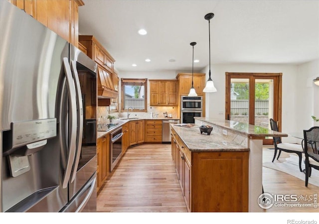 kitchen featuring appliances with stainless steel finishes, a sink, light wood-style flooring, and a center island