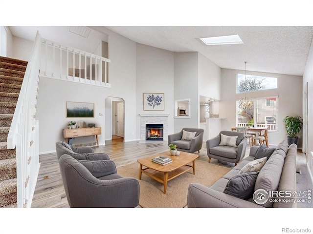 living room featuring wood finished floors, high vaulted ceiling, a notable chandelier, a glass covered fireplace, and stairs