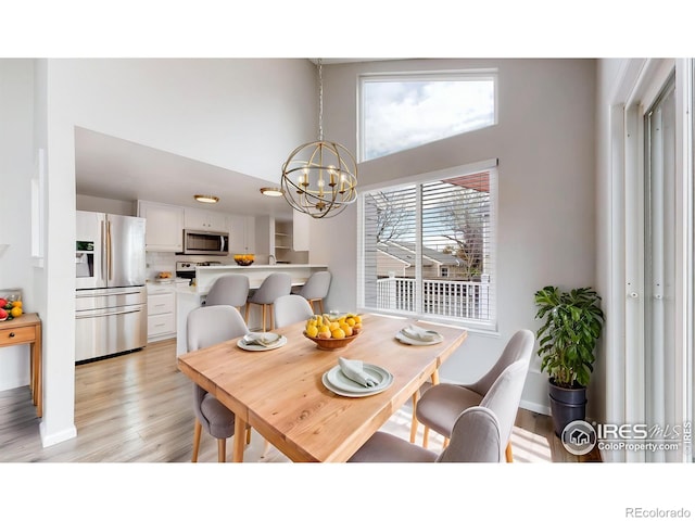 dining area featuring baseboards, light wood-style flooring, a high ceiling, and a notable chandelier