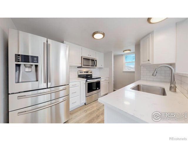 kitchen with a sink, appliances with stainless steel finishes, decorative backsplash, and white cabinetry