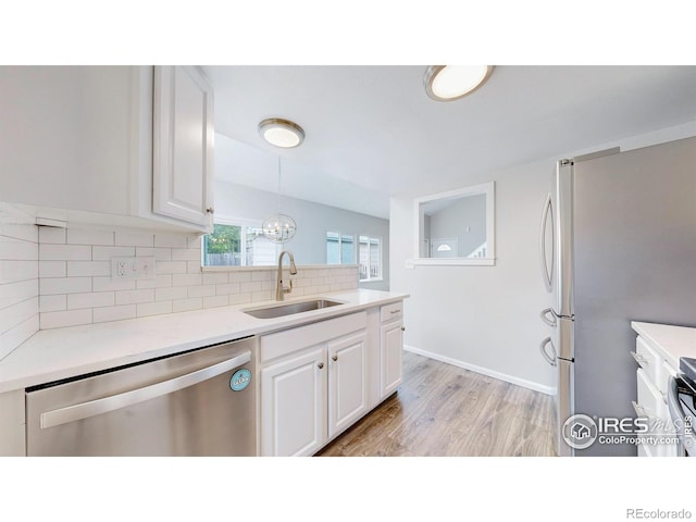 kitchen featuring appliances with stainless steel finishes, tasteful backsplash, a sink, light wood finished floors, and white cabinetry