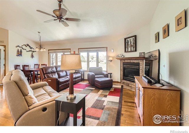 living area featuring vaulted ceiling, wood finished floors, ceiling fan with notable chandelier, and a glass covered fireplace
