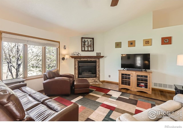 living area featuring lofted ceiling, wood finished floors, visible vents, a premium fireplace, and baseboards