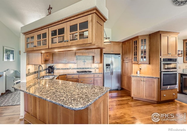 kitchen featuring lofted ceiling, stainless steel appliances, light wood-type flooring, and a sink