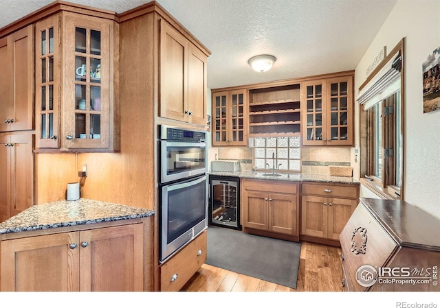kitchen with brown cabinets, a sink, double oven, light wood-type flooring, and wine cooler