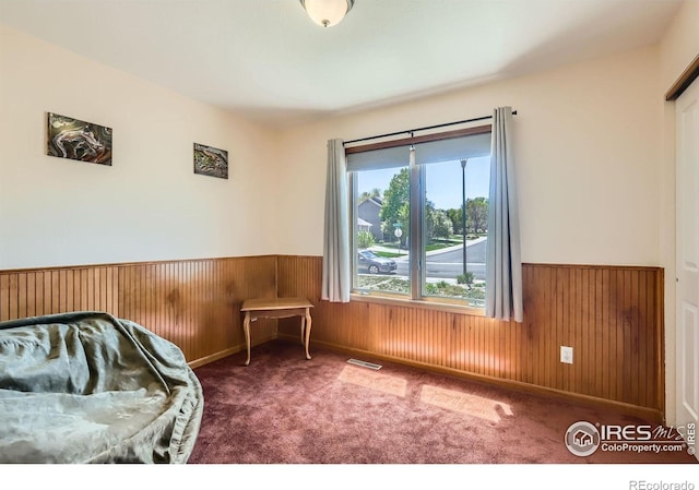 carpeted bedroom featuring wooden walls, wainscoting, and visible vents
