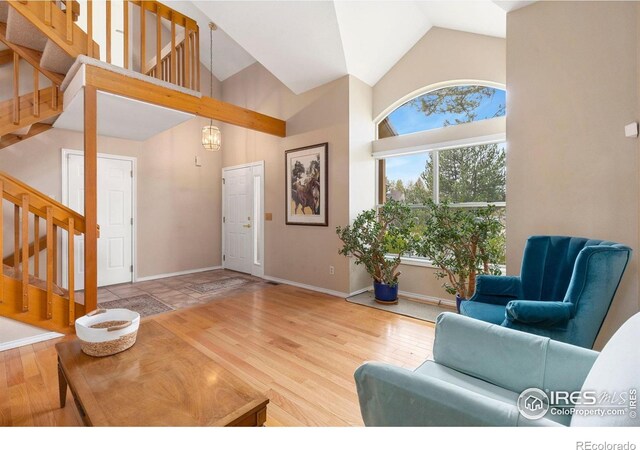 living room featuring baseboards, high vaulted ceiling, wood finished floors, and stairway