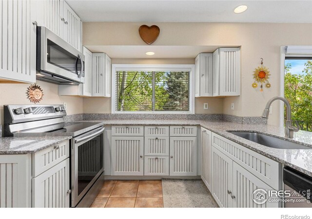 kitchen with stainless steel appliances, light tile patterned floors, a sink, and light stone counters