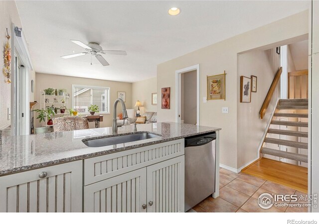 kitchen featuring a ceiling fan, stainless steel dishwasher, a sink, light tile patterned floors, and light stone counters