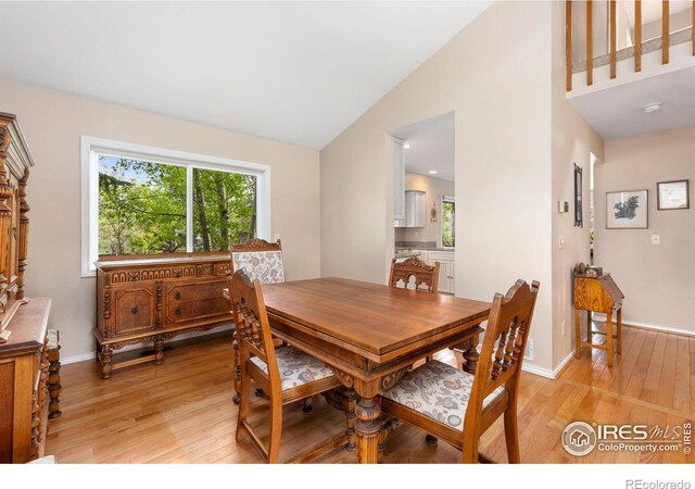 dining room featuring baseboards, light wood-style flooring, a wealth of natural light, and high vaulted ceiling