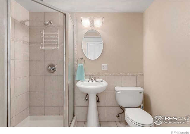 full bathroom with wainscoting, a sink, toilet, tile walls, and a shower stall