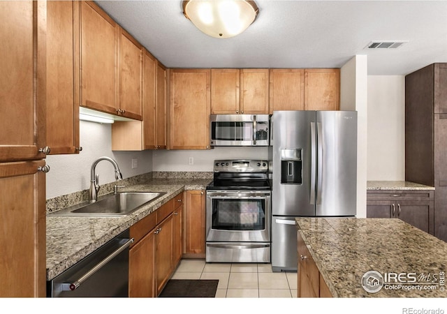 kitchen featuring visible vents, brown cabinetry, a sink, appliances with stainless steel finishes, and light tile patterned floors