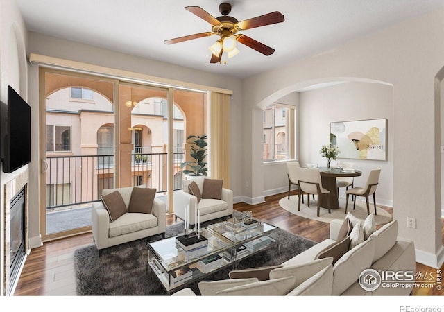 living room featuring arched walkways, ceiling fan, baseboards, and wood finished floors