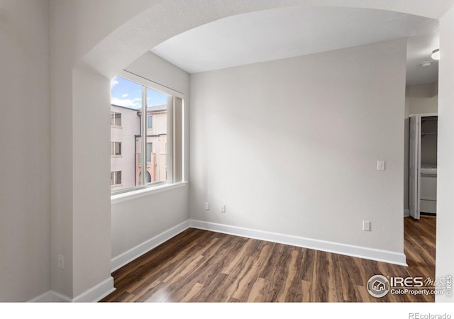 unfurnished room with arched walkways, baseboards, and wood finished floors