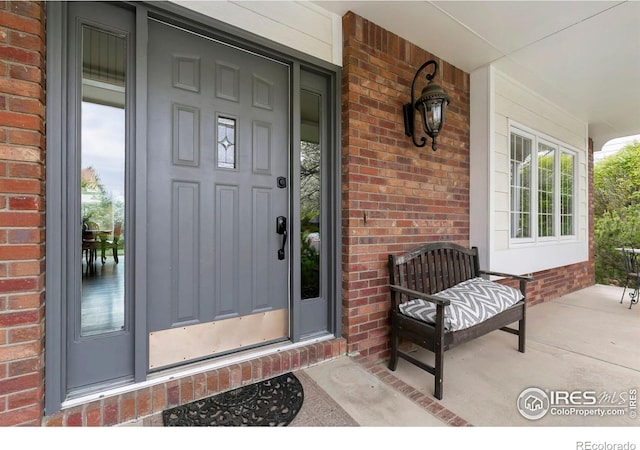 view of exterior entry with a porch and brick siding