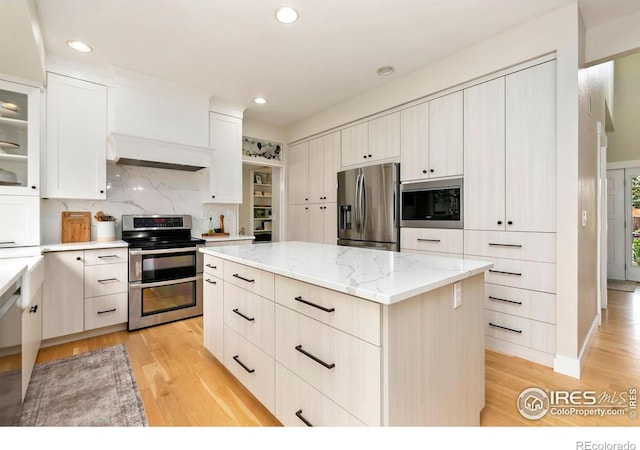 kitchen with light stone countertops, light wood finished floors, a center island, stainless steel appliances, and decorative backsplash