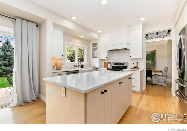 kitchen with a sink, light wood finished floors, stainless steel appliances, decorative backsplash, and a kitchen island