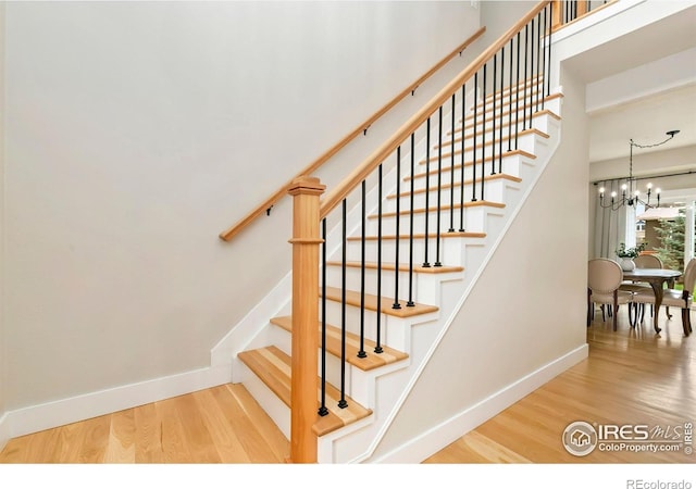 stairs featuring baseboards, wood finished floors, and a chandelier