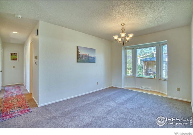 unfurnished room with an inviting chandelier, carpet floors, a textured ceiling, baseboards, and visible vents