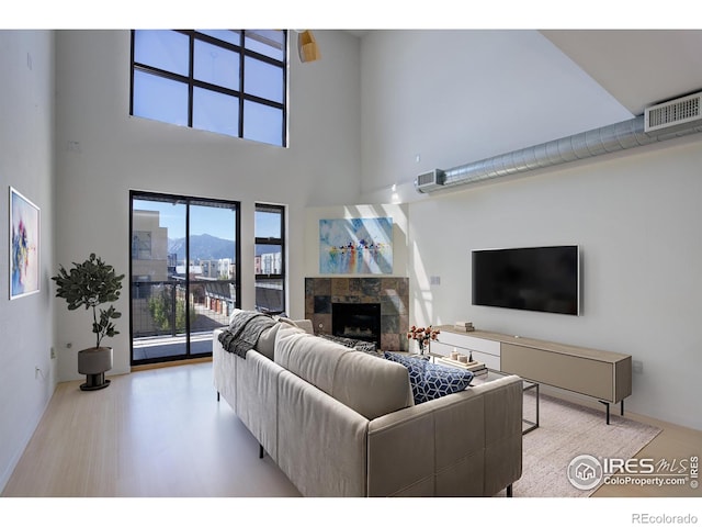 living room with a fireplace, visible vents, wood finished floors, and a towering ceiling