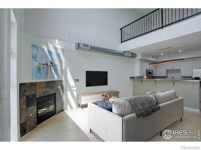 living area featuring a fireplace, visible vents, a towering ceiling, and light wood-type flooring