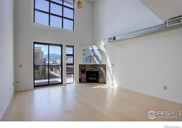 unfurnished living room featuring a tile fireplace, baseboards, wood finished floors, a towering ceiling, and visible vents