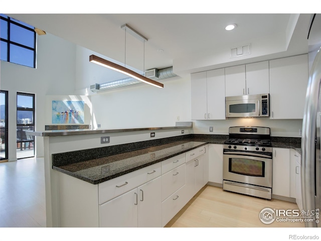 kitchen with visible vents, white cabinetry, a peninsula, stainless steel appliances, and light wood-style flooring