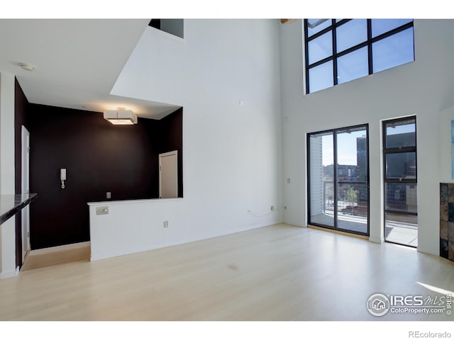 unfurnished living room with a towering ceiling, wood finished floors, and a healthy amount of sunlight