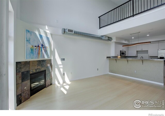 unfurnished living room with visible vents, baseboards, a high ceiling, a tile fireplace, and light wood-style flooring